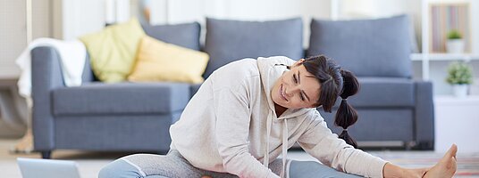 Eine junge Frau macht vor dem Laptop Gymnastik