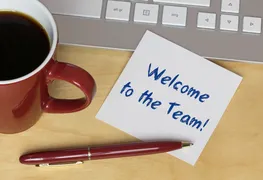 Kaffeetasse, Tastatur und ein Post-it mit "Welcome to the team"